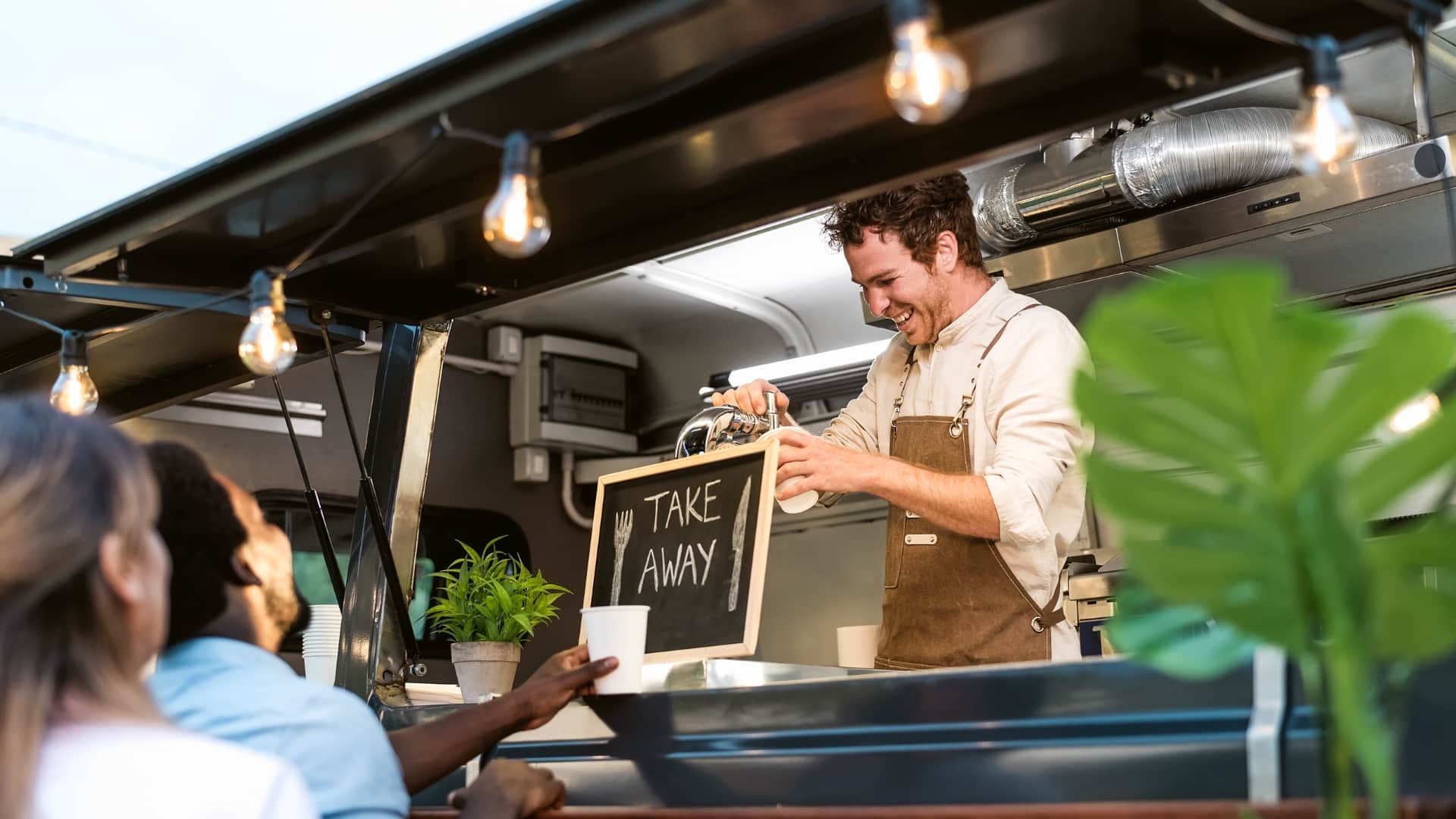 People being served at a food truck. A chalkboard sign reads 'take away'.